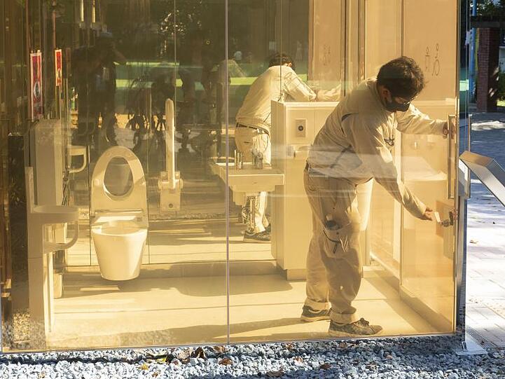 Ein Mann schließt die Tür einer neu installierten öffentlichen Toilette mit transparenten Wänden, die im Yoyogi Fukamachi Mini Park im Bezirk Shibuya steht. Die drei Toiletten aus transparentem Glas werden undurchsichtig, sobald jemand eintritt und die Tür verschließt.