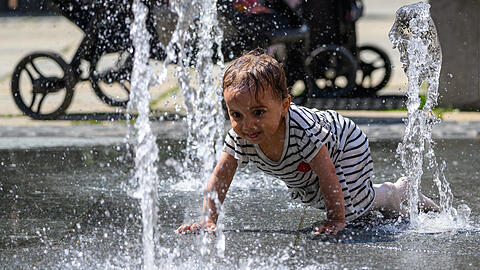 13.08.2025, Sachsen, Chemnitz: Die einj&auml;hrige Ayat krabbelt im Zentrum von Chemnitz durch die Wasserstrahlen eines Springbrunnens. Bei Temperaturen um 30 Grad Celsius bieten die Wasserspiele eine willkommene Abk&uuml;hlung. Foto: Hendrik Schmidt/dpa +++ dpa-Bildfunk +++