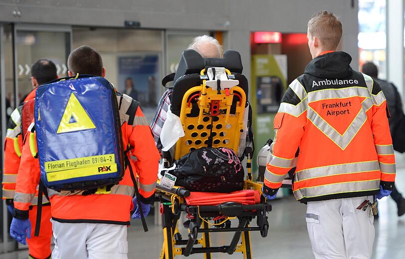 Ein Passagier erleitet in der Warteschlange einen Schwächeanfall. Ersthelfer bringen ihn in den Sanitätsbereich.
