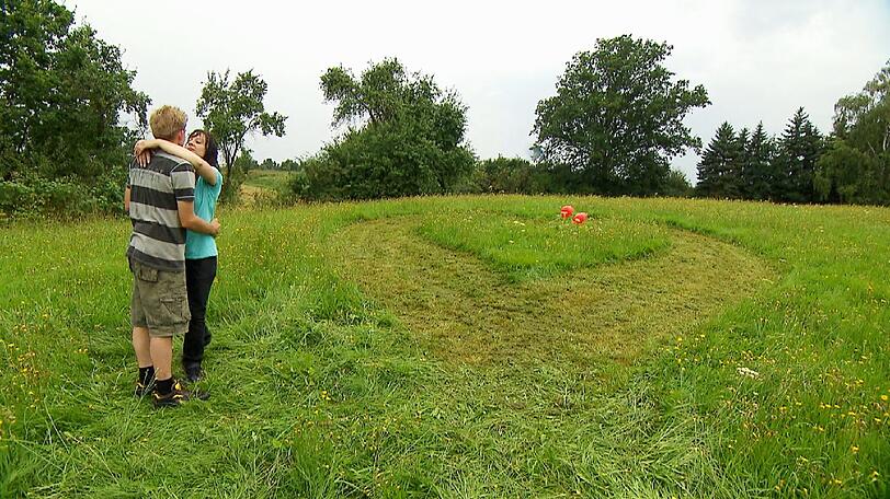 Hühner- und Schweinebauer Rolf (28) hat für Janine (35) ein Herz in die Wiese mäht. Janine ist von der romantischen Liebeserklärung tief berührt.