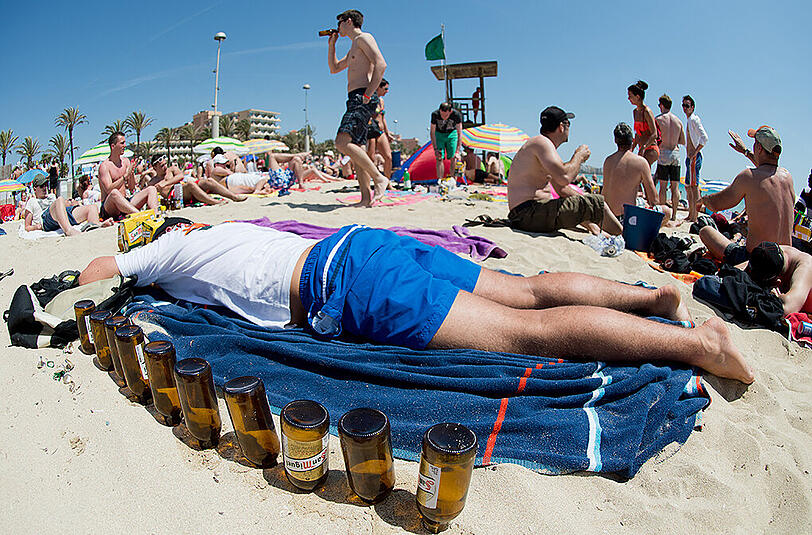 Ausgetrunken: Ein Tourist schläft neben leeren Bierflaschen am Strand von Arenal. Foto: Julian Stratenschulte/Archiv