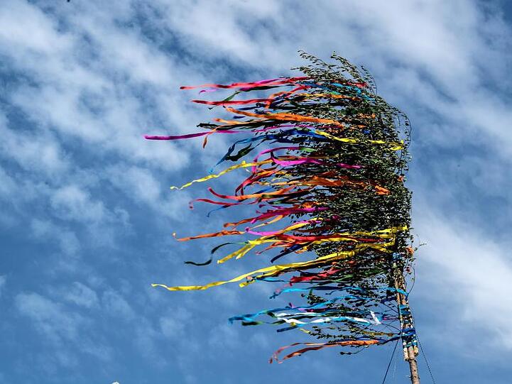 Die bunten Bänder eines Maibaumes flattern vor dem blauen Himmel. Foto: picture alliance / Federico Gambarini/dpa/Archivbild