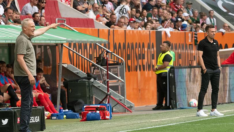Freiburgs Trainer Christian Streich (l) und Augsburgs Trainer Enrico Maaßen geben ihren Spielern an der Seitenlinie Anweisungen.