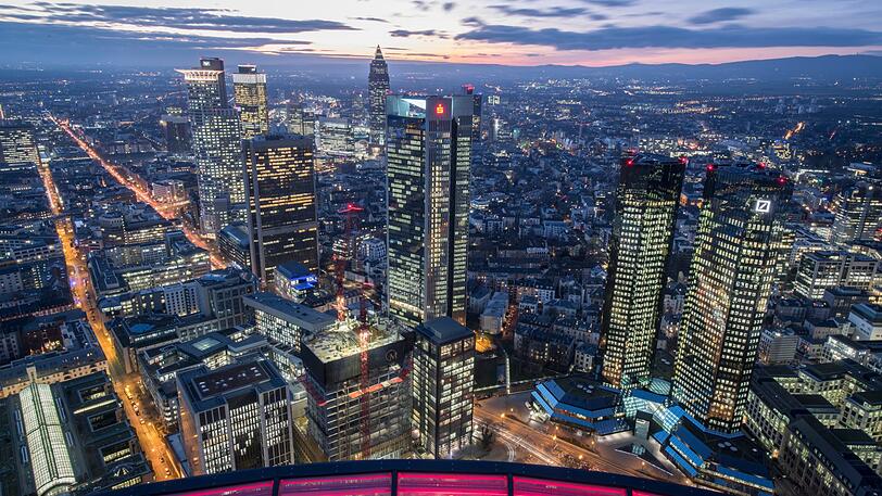 Frankfurt am Main: Die rot beleuchtete Glaseinfassung des Maintower umrahmt den Blick auf die Bankenskyline. Dabei steht rechts der Doppelturm der Deutschen Bank, links daneben der Sparkassenturm, in der Bildmitte der Messeturm mit seiner charakteristischen Pyramidenspitze.