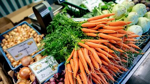 Karotten und Zwiebeln an einem Obst- und Gemüsestand auf einem Wochenmarkt. Die Preise für Nahrungsmittel bleiben weiter hoch.