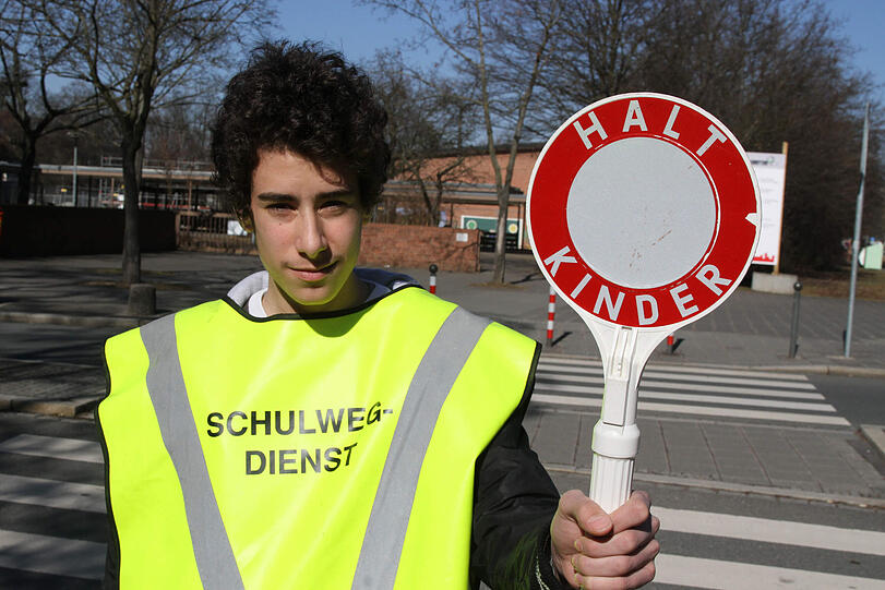 &bdquo;Halt Kinder&ldquo; steht auf der Kelle: Pasquale hilft als Schülerlotse im neonfarbenen Umhang an seiner Schule in der Ossietzkystraße den Kleinen über die Straße.