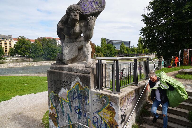 Der Aktionskünstler hat sich den Beutel über die Schultern gehievt und trägt den Müll zu einer städtischen Gitterbox.