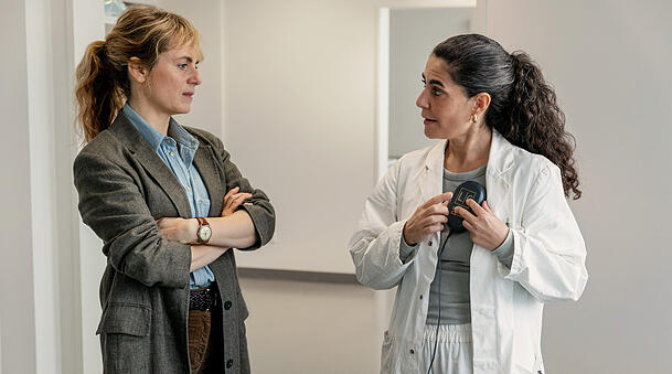Dr. Şahin erklärt, wie das Update eines ICD-Geräts funktioniert: Kommissarin Isabelle Grandjean (Anna Pieri Zuercher) und Dr. Esme Şahin (Beren Tuna).