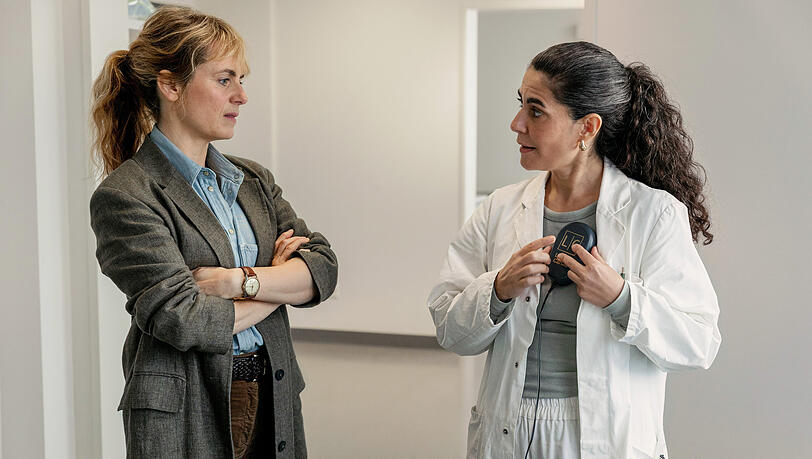 Dr. Şahin erklärt, wie das Update eines ICD-Geräts funktioniert: Kommissarin Isabelle Grandjean (Anna Pieri Zuercher) und Dr. Esme Şahin (Beren Tuna).