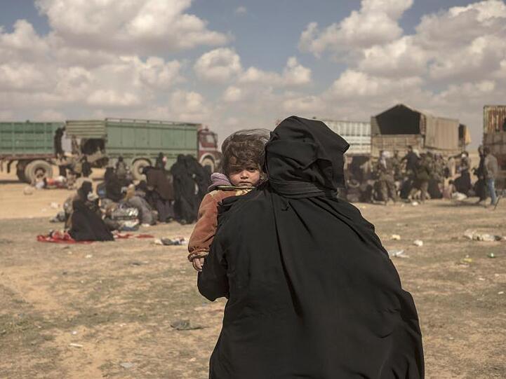 Eine Frau trägt ihr Kind durch ein Lager im syrischen Baghus, in dem Angehörige von IS-Kämpfern untergebracht sind.