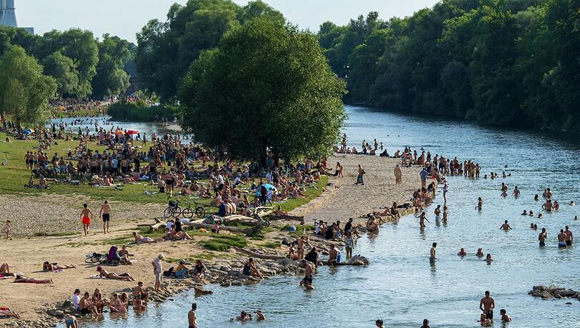 Menschen genießen das gute Wetter am Isarufer. Nicht nur Abkühlen im Wasser hilft gegen die Hitze.