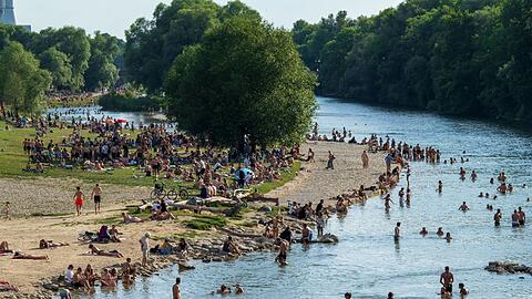 Menschen genießen das gute Wetter am Isarufer. Nicht nur Abkühlen im Wasser hilft gegen die Hitze.