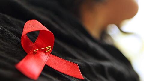Eine Frau trägt eine rote Schleife, ein Symbol der Solidarität mit Menschen mit HIV oder Aids. Foto: Oliver Berg/dpa/Archivbild