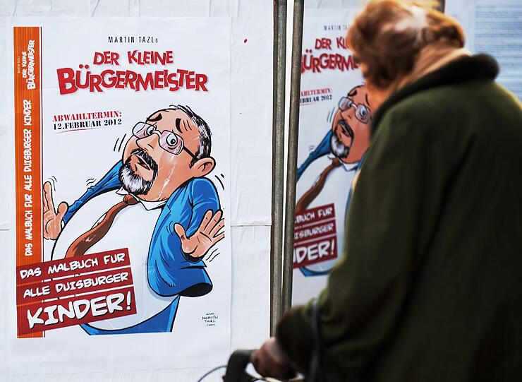 Passanten betrachten am Donnerstag in Duisburg eine Karikatur des Kuenstlers Martin Tazl vom Oberbuergermeister von Duisburg, Adolf Sauerland (CDU), mit der Ueberschrift "Duisburg bin ich!" und der Unterschrift "Nicht mehr lange!!!"