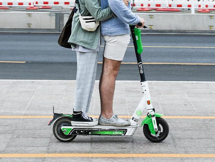 Zwei Personen fahren gemeinsam auf einem E-Tretroller. Foto: Jens Kalaene