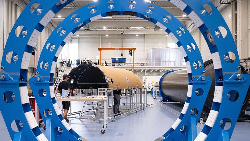 Mitarbeiter des Raumfahrtunternehmens Isar Aerospace fertigen in einer Halle die Verkleidung einer Rakete.