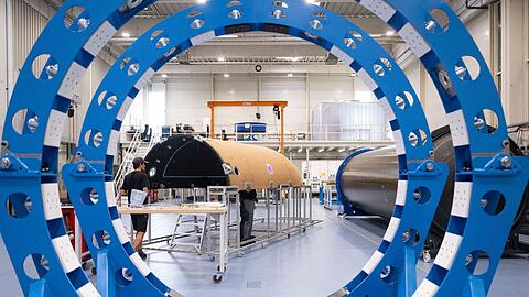 Mitarbeiter des Raumfahrtunternehmens Isar Aerospace fertigen in einer Halle die Verkleidung einer Rakete.
