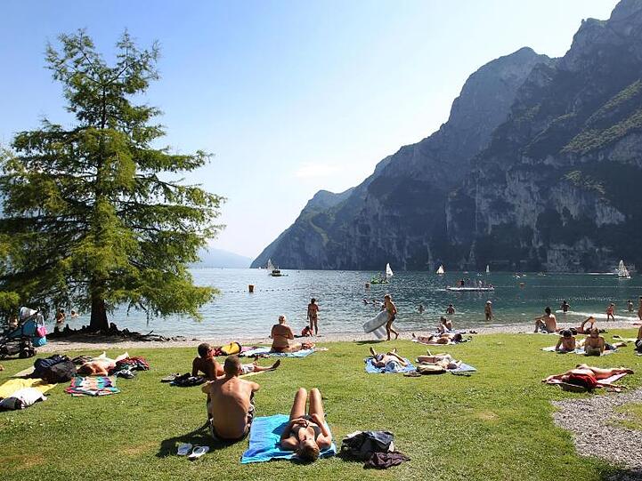 Touristen und Einheimische nehmen am Strand von Riva del Garda ein Sonnenbad. Foto: picture alliance / dpa / Archivbild
