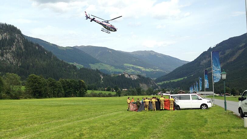 Ein Rettungshelikopter fliegt über ein Feld in Krimml, während Einsatzkräfte an einem Auto stehen. Ein Rettungshelikopter fliegt über ein Feld in Krimml, während Einsatzkräfte an einem Auto stehen.