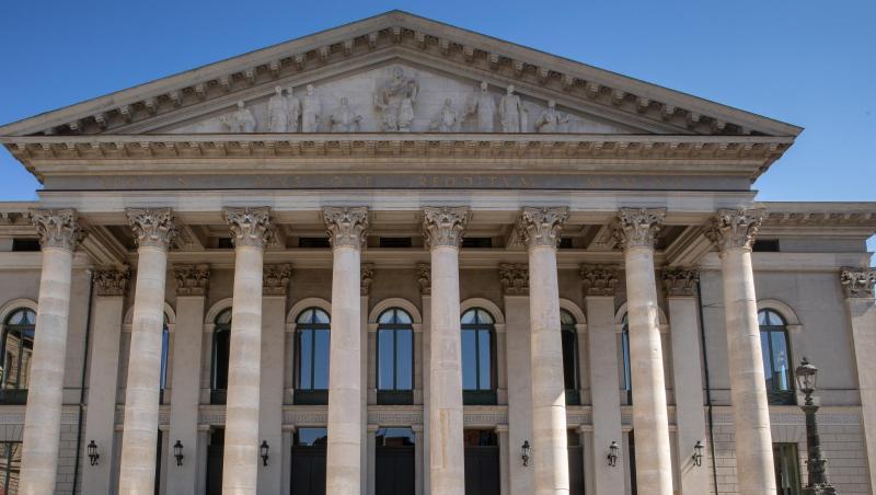 Passanten sitzen auf der Treppe vor der Bayerischen Staatsoper.