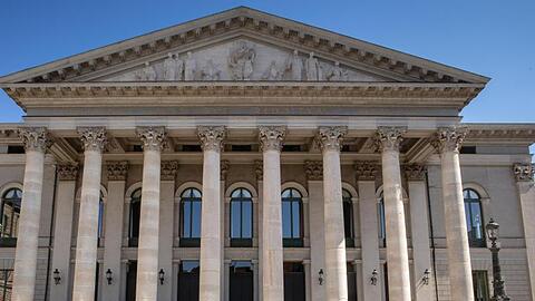 Passanten sitzen auf der Treppe vor der Bayerischen Staatsoper.