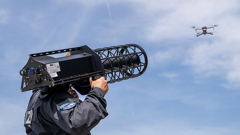 Ein Polizist visiert mit einem Abwährgerät eine Drohne am Himmel an. Ein Polizist visiert mit einem Abwährgerät eine Drohne am Himmel an.