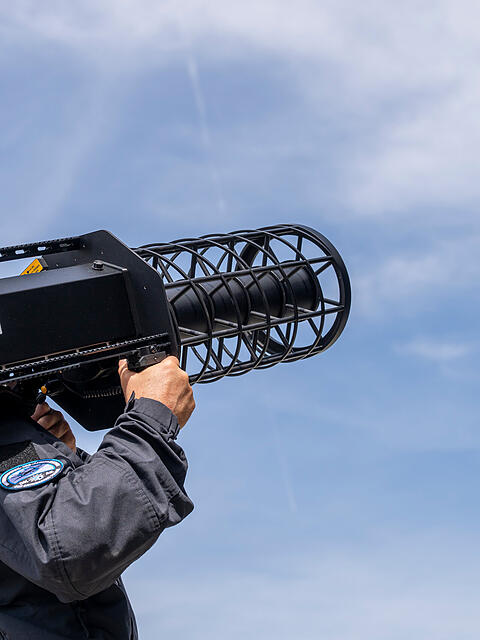 Ein Polizist visiert mit einem Abw&auml;hrger&auml;t eine Drohne am Himmel an.