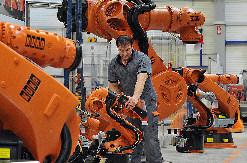 Ein Arbeiter kontrolliert in Augsburg (Bayern) einen Roboter von Kuka.