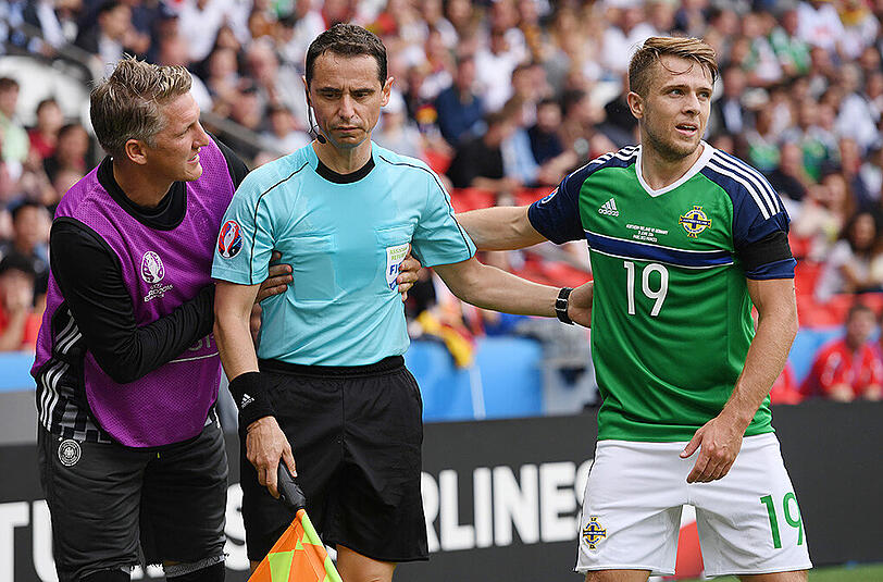 Bastian Schweinsteiger und Nordirlands Jamie Ward (rechts) helfen dem französischen Schiedsrichter-Assistenten Fréderic Cano (Mitte) auf die Beine.