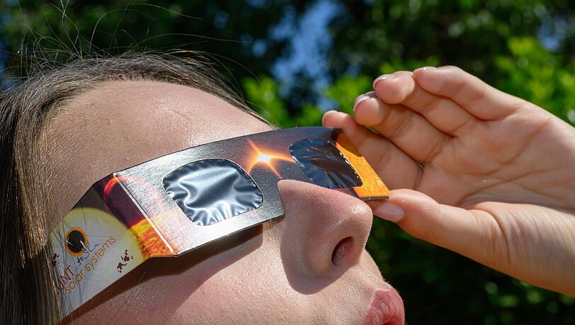 Eine junge Frau schaut durch eine Sonnenfinsternisbrille und betrachtet die Mittagssonne. Eine junge Frau schaut durch eine Sonnenfinsternisbrille und betrachtet die Mittagssonne.