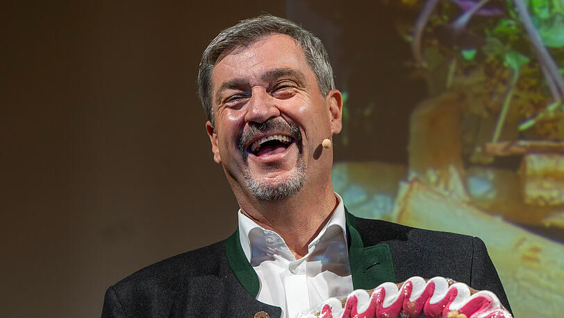 Feixend hält der Ministerpräsident von Bayern ein Lebkuchenherz mit der Aufschrift "#Cathy kocht - #Söder isst Das Nicht" in die Kamera. Feixend hält der Ministerpräsident von Bayern ein Lebkuchenherz mit der Aufschrift "#Cathy kocht - #Söder isst Das Nicht" in die Kamera.