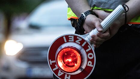 Ein Polizist hält bei einer Verkehrskontrolle eine Winkerkelle in der Hand.