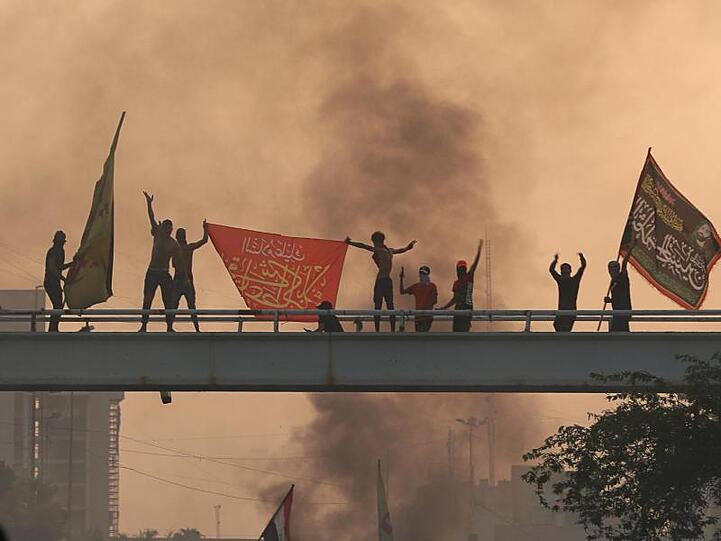 Eine Gruppe Demonstranten schwenken auf einer Brücke Fahnen. Den zweiten Tag infolge sind irakische Sicherheitskräfte in der Hauptstadt Bagdad mit Gewalt gegen Proteste vorgegangen.