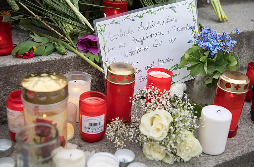 Blumen und Kerzen liegen am Bahnhof in Grafing um ein handgemaltes Schild. Bei einer Messerattacke waren am Dienstag drei Personen verletzt und ein Mann getötet worden.