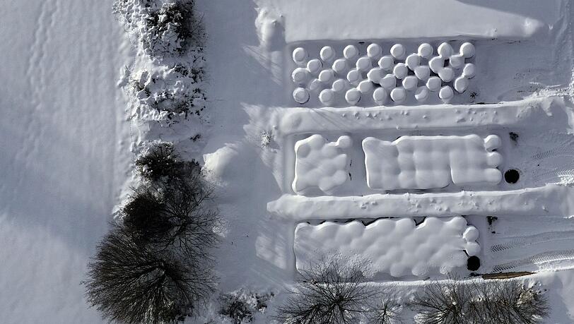 Schneebedeckte Silageballen liegen von einer Hecke umgeben auf einem Hof (Luftaufnahme mit einer Drohne).