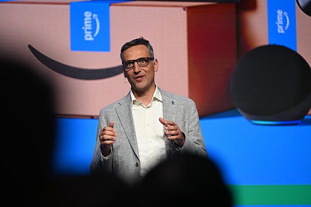 Der Amazon-Deutschlandchef, Rocco Bräuniger, steht bei einer Präsentation von Amazon in einem Logistikstandort des US-Konzerns auf einer Bühne vor einer Leinwand und spricht zu Journalisten und Mitarbeitenden. Der Amazon-Deutschlandchef, Rocco Bräuniger, steht bei einer Präsentation von Amazon in einem Logistikstandort des US-Konzerns auf einer Bühne vor einer Leinwand und spricht zu Journalisten und Mitarbeitenden.