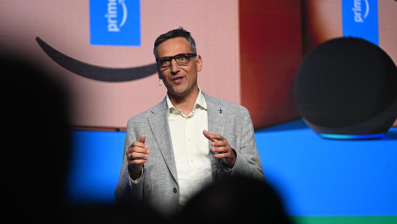 Der Amazon-Deutschlandchef, Rocco Bräuniger, steht bei einer Präsentation von Amazon in einem Logistikstandort des US-Konzerns auf einer Bühne vor einer Leinwand und spricht zu Journalisten und Mitarbeitenden. Der Amazon-Deutschlandchef, Rocco Bräuniger, steht bei einer Präsentation von Amazon in einem Logistikstandort des US-Konzerns auf einer Bühne vor einer Leinwand und spricht zu Journalisten und Mitarbeitenden.