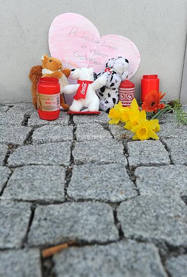 Blumen, Kerzen, Stofftiere und ein Papierherz mit der Aufschrift "Du bleibst immer in unseren Gedanken" liegen in Unterföhring vor einem Hauseingang an Gedenken an die ermordete Larissa.