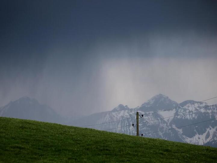 Wolken regnen am Alpenrand über den Bergen ab. Foto: Karl-Josef Hildenbrand/dpa/Symbolbild