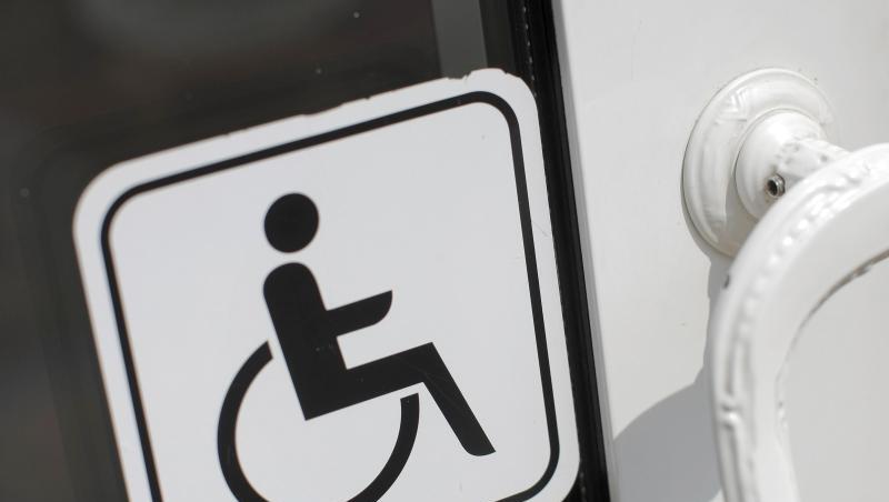 An einer Tür klebt ein Hinweisschild für Menschen mit Behinderung.