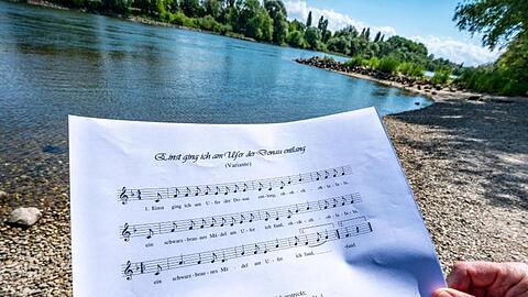 Ein Notenblatt mit dem Liedtext &bdquo;Einst ging ich am Ufer der Donau entlang&ldquo; wird am Donauufer gehalten. Foto: Armin Weigel/dpa/Archivbild
