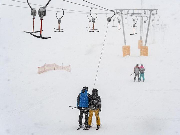 Wintersportler fahren mit einem Skilift im Schneegestöber. Foto: Armin Weigel/Archiv