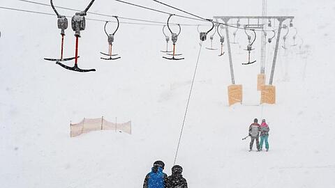 Wintersportler fahren mit einem Skilift im Schneegestöber. Foto: Armin Weigel/Archiv