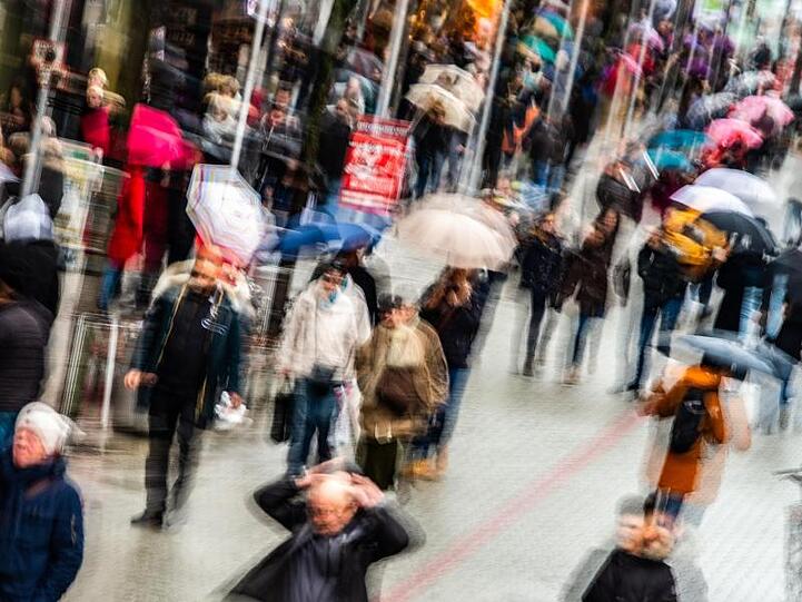 Passanten mit Einkaufstüten gehen durch eine Fußgängerzone.