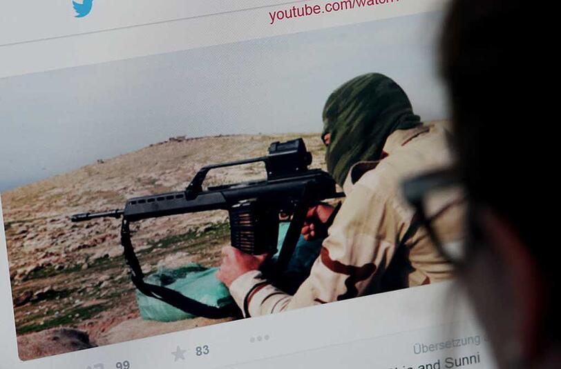 Eine junge Frau schaut auf einen Computermonitor, auf dem eine Website mit Propaganda des IS zu sehen ist.