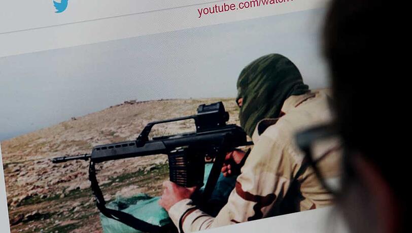 Eine junge Frau schaut auf einen Computermonitor, auf dem eine Website mit Propaganda des IS zu sehen ist. Eine junge Frau schaut auf einen Computermonitor, auf dem eine Website mit Propaganda des IS zu sehen ist.