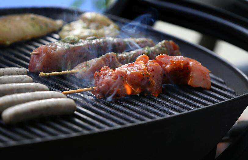 Fleischspieße, Bratwürste und Steaks liegen auf dem Rost eines Gasgrills.