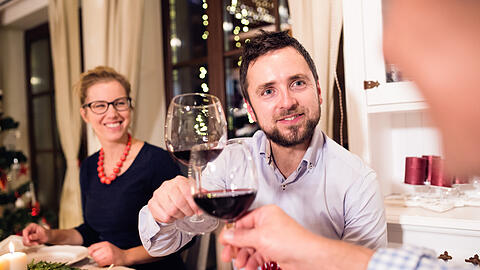 Beautiful young couple celebrating Christmat together with their family, clinking with wine glasses.