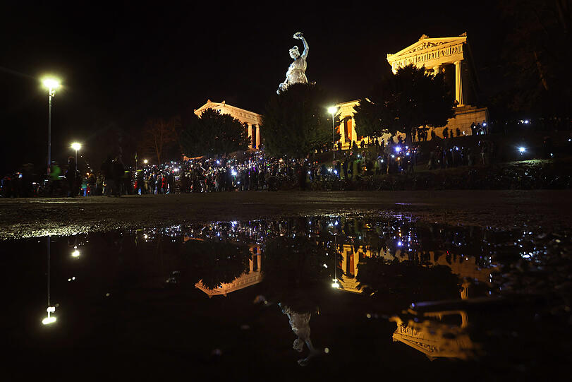 "Lichtermeer für Demokratie, gegen Rassismus, Antisemitismus und Hetze": Demonstranten unter der Ruhmeshalle und der Bavaria spiegeln sich auf der Theresienwiese in einer Regenpfütze.