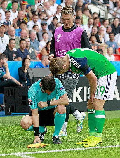 Bastian Schweinsteiger und Nordirlands Jamie Ward (rechts) helfen dem französischen Schiedsrichter-Assistenten Fréderic Cano (Mitte) auf die Beine.
